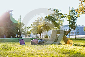 Mid adult thoughtful businessman lying on the grass in park with his laptop