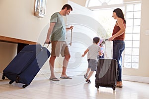 Mid adult white couple and kids leaving their home with luggage to go on vacation, full length