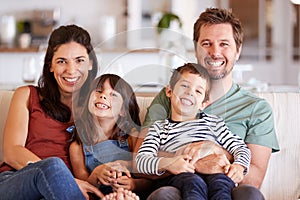 Mid adult white couple and their two young children sitting on a sofa at home smiling to camera