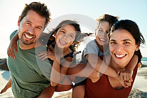 Mid adult white parents piggybacking their kids on a beach, smiling to camera, close up, backlit photo