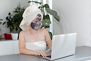 Mid adult woman in clay facial mask wearing bath towel using her laptop.