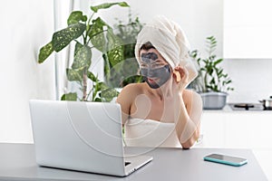 Mid adult woman in clay facial mask wearing bath towel using her laptop.