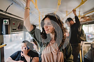 Mid adult woman commuter is standing in bus and travelling in public transport.