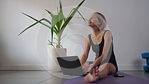 Mid adult woman doing yoga with tutorial on the laptop