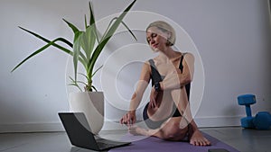 Mid adult woman doing yoga with tutorial on the laptop