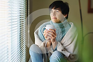 Mid adult woman drinking coffee and looking out of the window in winter day.