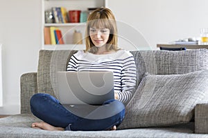 Mid adult woman on her sofa using laptop at home.