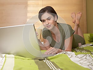 Mid-adult woman looking at computer in bed