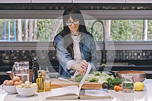 Mid-adult woman reading recipe while preparing food in the kitchen
