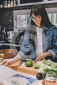Mid-adult woman reading recipe while preparing food in the kitchen. Vertical shot