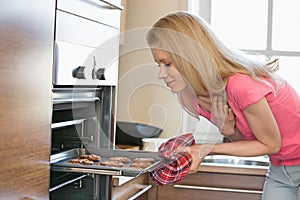 Mid adult woman removing baking tray from oven in kitchen