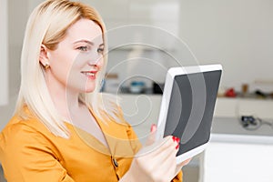 Mid adult woman sitting on sofa with tablet pc. Horizontal shape, front view, copy space