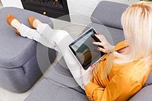 Mid adult woman sitting on sofa with tablet pc. Horizontal shape, front view, copy space