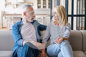 Mid age couple enjoy conversation sitting on sofa in living room