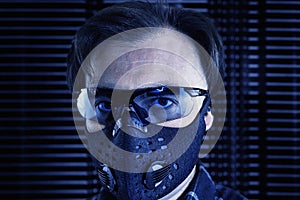 A mid age man in sunglasses and a respiratory mask on a futuristic metal background