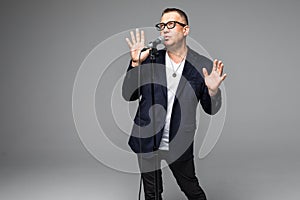 The mid age Showman interviewer with emotions. Young elegant mature man holding microphone against white background. Showman conce