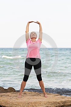Mid age woman stretching on the beach. Yoga concept
