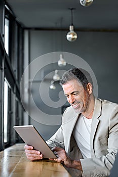 Mid aged business man using digital tablet computer sitting in modern office.
