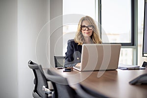 Mid aged businesswoman with notebook sitting at desk in a modern office and working