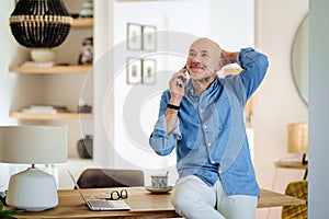 Mid aged casual businessman sitting at desk and making a call at home