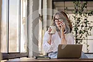 Mid aged entrepreneur female having a call and using notebook at home