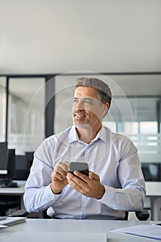 Mid aged happy business man using mobile phone in office thinking, vertical.