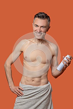 A mid aged man with a deo spray looking cheerful after shower