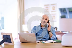 Mid aged man sitting at home and using his smartphone and notebook for work