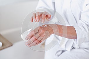 Mid aged woman applying moisturizer cream on hands