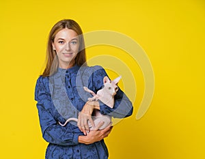 Mid-aged woman, dedicated cat lover, radiates happiness as lovingly holds content and happy cat in hands against yellow