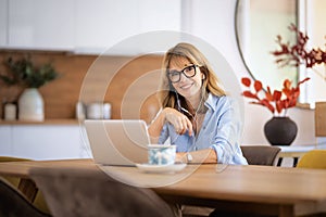 Mid aged woman with earphone, using laptop and having video call at home