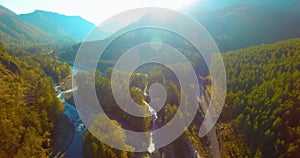 Mid air flight over fresh mountain river and meadow at sunny summer morning. Rural dirt road below.