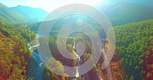 Mid air flight over fresh mountain river and meadow at sunny summer morning. Rural dirt road below.