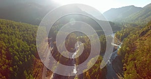 Mid air flight over fresh mountain river and meadow at sunny summer morning. Rural dirt road below.