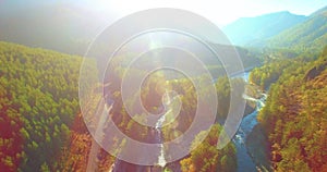 Mid air flight over fresh mountain river and meadow at sunny summer morning. Rural dirt road below.