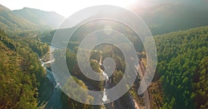 Mid air flight over fresh mountain river and meadow at sunny summer morning. Rural dirt road below.