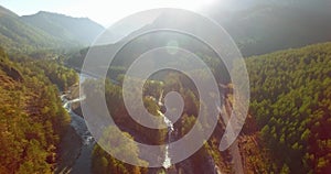 Mid air flight over fresh mountain river and meadow at sunny summer morning. Rural dirt road below.