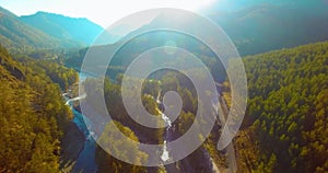 Mid air flight over fresh mountain river and meadow at sunny summer morning. Rural dirt road below.