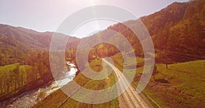 Mid air flight over fresh mountain river and meadow at sunny summer morning. Rural dirt road below. Cows and car.