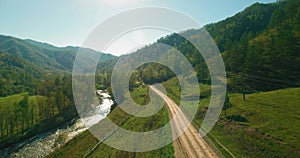 Mid air flight over fresh mountain river and meadow at sunny summer morning. Rural dirt road below. Cows and car.