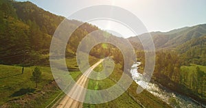 Mid air flight over fresh mountain river and meadow at sunny summer morning. Rural dirt road below. Cows and car.