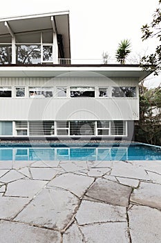 Mid century home exterior with blue tiled swimming pool and crazy paving