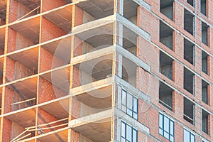 Mid-construction high-rise building with exposed steel beams, concrete sections, installed windows reflecting light, rough and