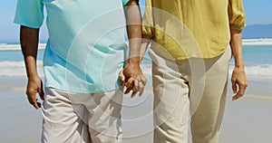 Mid section of active senior African American couple holding hands and walking on the beach 4k