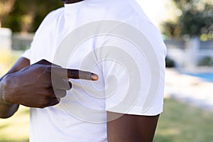 Mid section of african american man in white t-shirt pointing at sleeve with copy space in garden photo