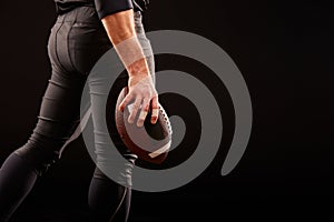 Mid section of American football player with ball against black, copy space, side view