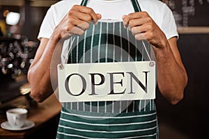 Mid section of barista holding open sign