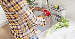 Mid section of biracial man rinsing vegetables in kitchen, slow motion