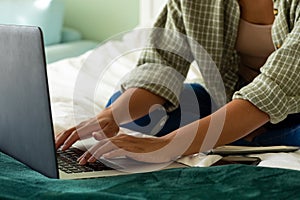 Mid section of biracial woman using laptop and smartphone on bed in bedroom