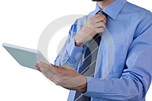 Mid section of businessman adjusting necktie while holding tablet